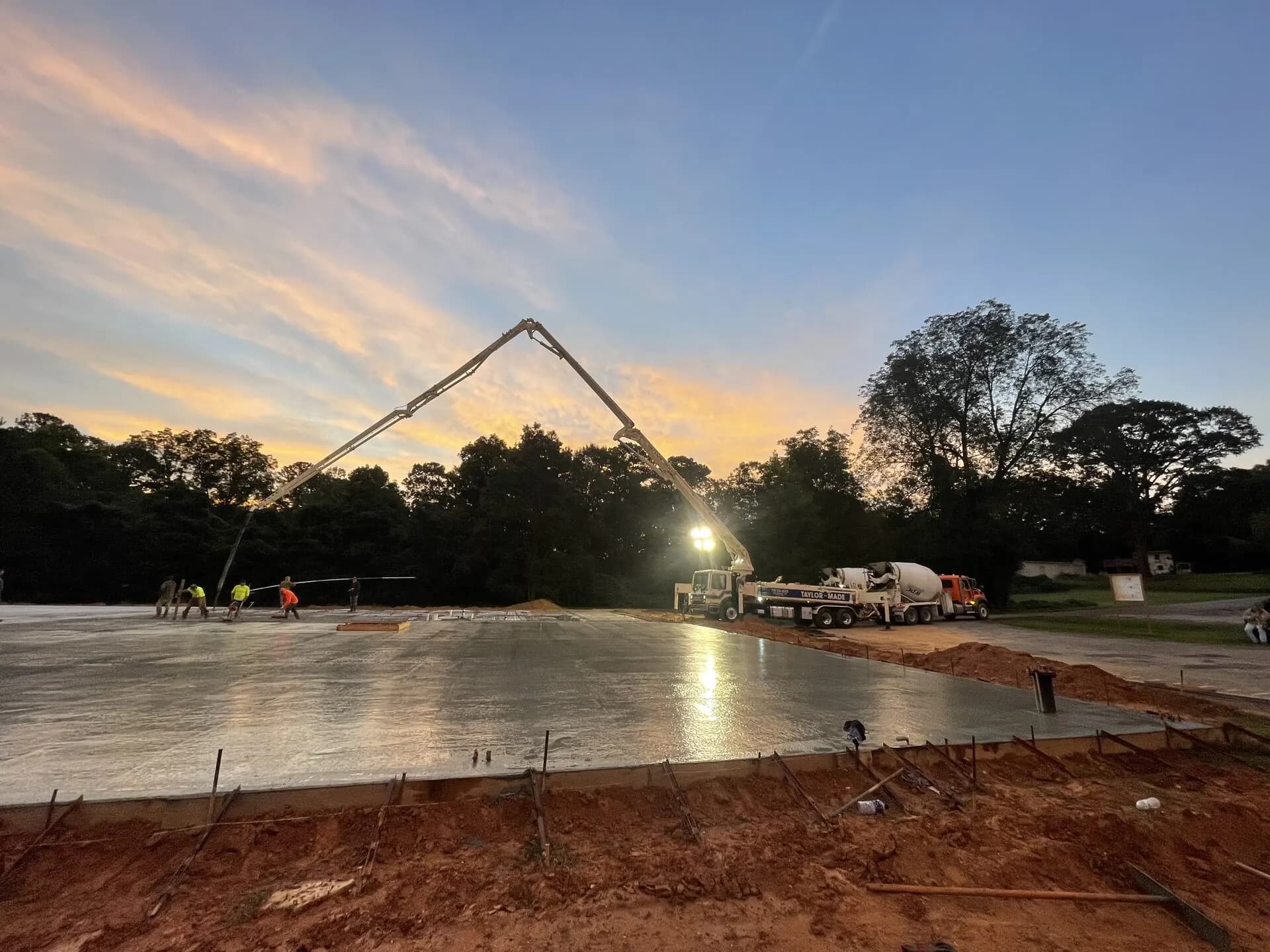 Concrete crew pouring a commercial slab at sunrise with a boom pump truck